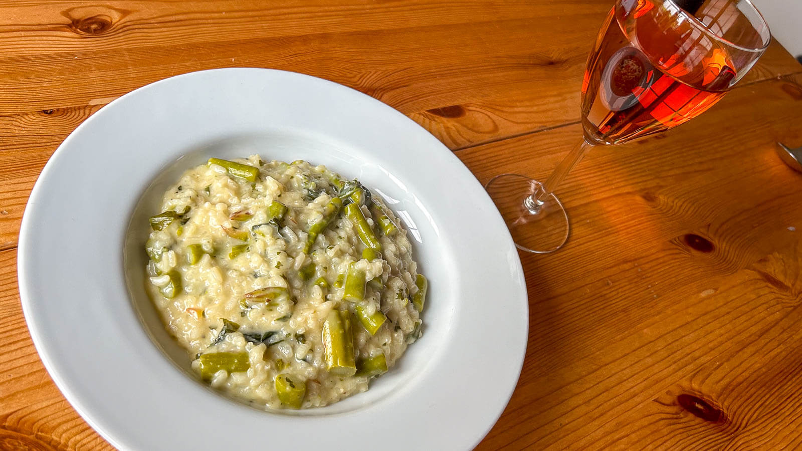 Barlach Risotto mit grünem Spargel angerichtet auf Teller neben einem Glas Wein.