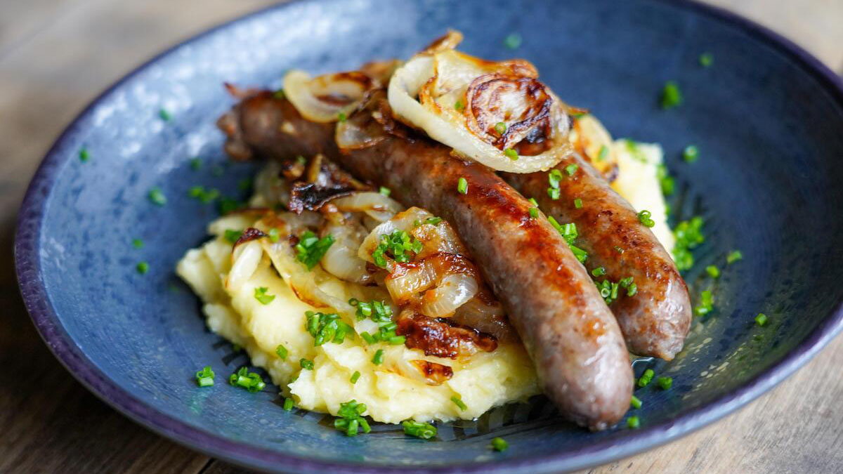 Wildbratwürste angerichtet auf Kartoffelpüree auf einem blauen Porzellanteller