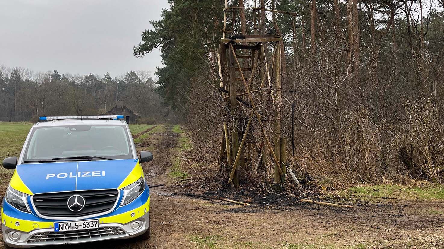 Ein Polizeiauto steht neben einem abgebrannten Hochsitz an einem Waldrand.